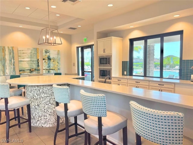 kitchen featuring a kitchen breakfast bar, decorative light fixtures, an inviting chandelier, white cabinets, and stainless steel microwave