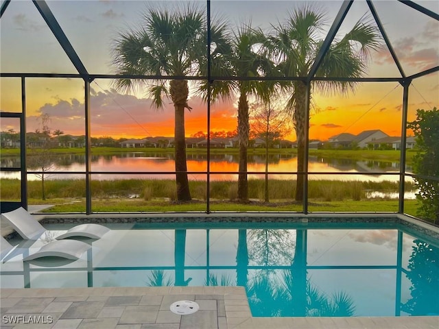 pool at dusk featuring a water view and a lanai