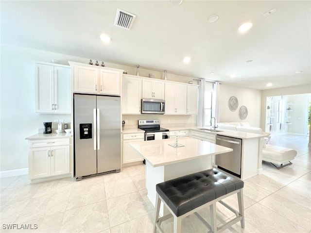 kitchen with kitchen peninsula, stainless steel appliances, sink, white cabinets, and a kitchen island