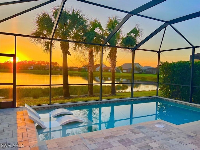 pool at dusk with a lanai, a patio area, a water view, and a hot tub