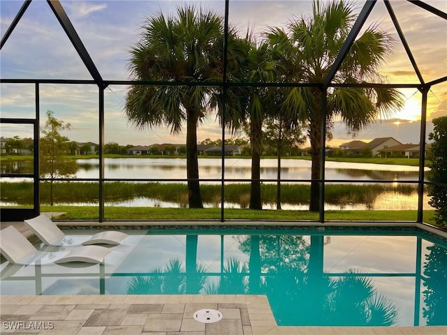 pool at dusk featuring glass enclosure and a water view