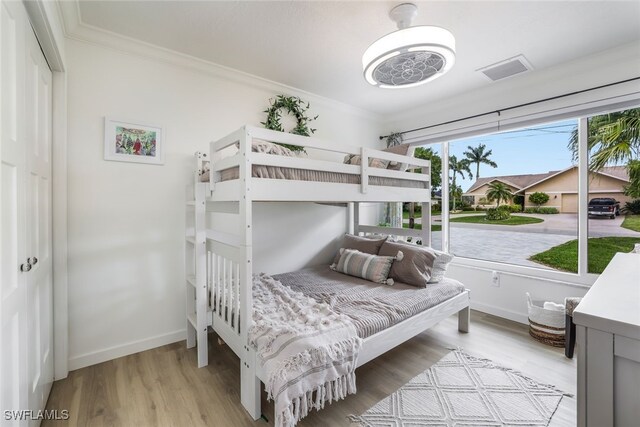 bedroom with ornamental molding, light wood-type flooring, and multiple windows