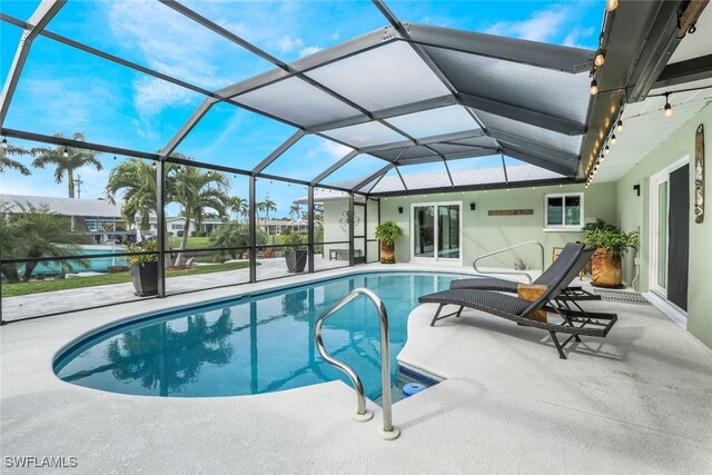 view of pool featuring glass enclosure, a patio area, and a water view