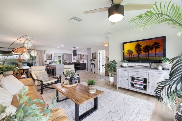 living room with crown molding, ceiling fan, and light hardwood / wood-style floors