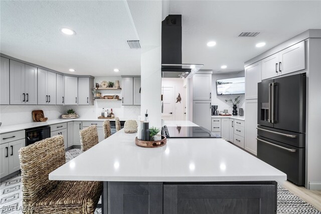 kitchen featuring black appliances, gray cabinetry, wall chimney range hood, and a kitchen island