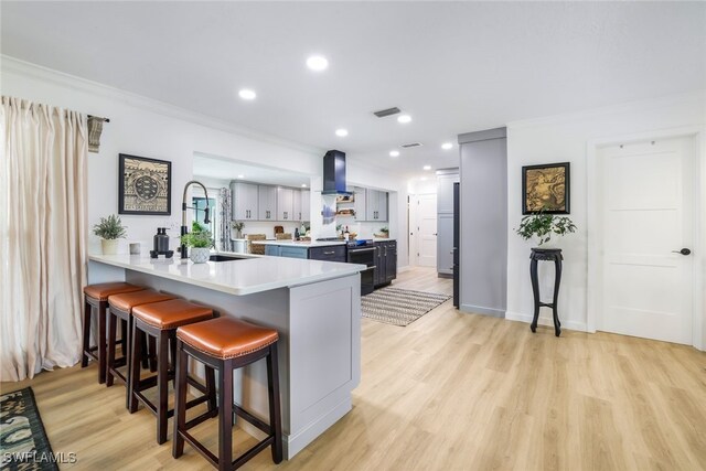 kitchen featuring light wood-type flooring, wall chimney range hood, kitchen peninsula, a breakfast bar, and ornamental molding