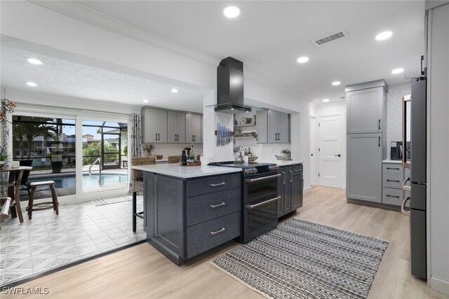 kitchen featuring light hardwood / wood-style flooring, stainless steel appliances, gray cabinetry, and wall chimney exhaust hood