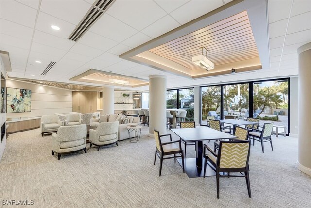 carpeted dining space with a raised ceiling and decorative columns