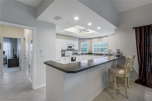 kitchen with kitchen peninsula, ceiling fan, white cabinets, white appliances, and a breakfast bar