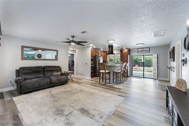 living room with light wood-type flooring, ceiling fan, and a textured ceiling