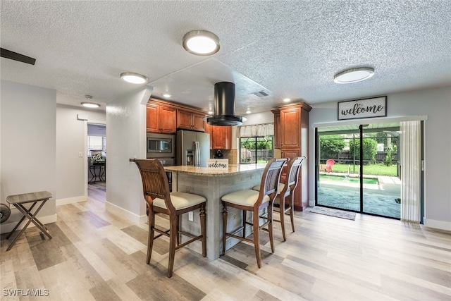 kitchen featuring appliances with stainless steel finishes, a kitchen breakfast bar, a textured ceiling, and light hardwood / wood-style flooring