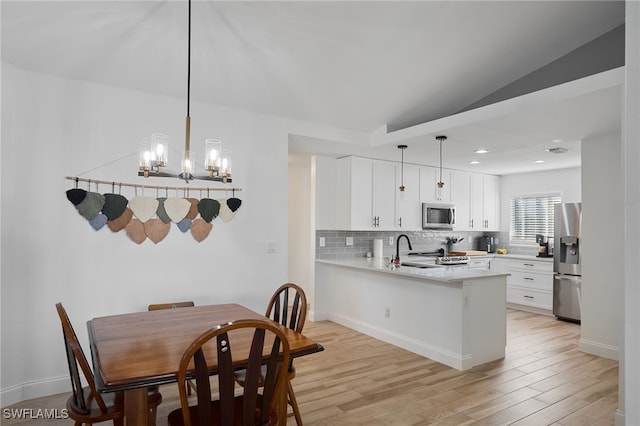 dining room with sink, light hardwood / wood-style flooring, a chandelier, and vaulted ceiling