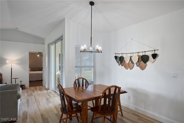 dining area with light wood-type flooring, an inviting chandelier, and vaulted ceiling