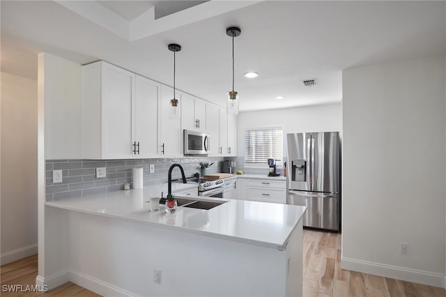 kitchen featuring white cabinetry, kitchen peninsula, appliances with stainless steel finishes, decorative backsplash, and decorative light fixtures