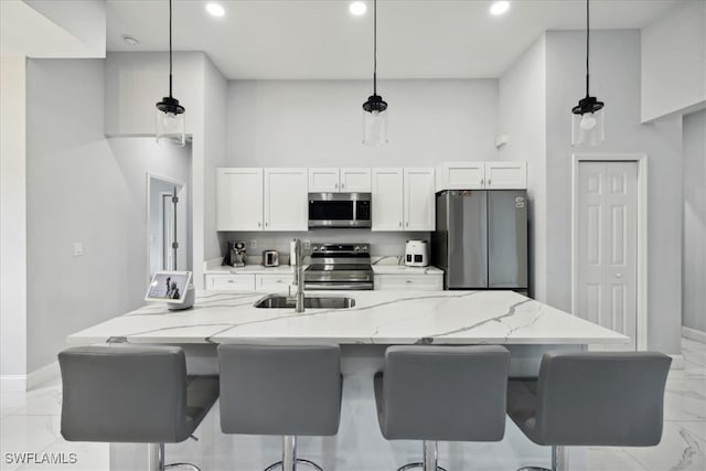 kitchen featuring white cabinets, decorative light fixtures, appliances with stainless steel finishes, light stone countertops, and sink