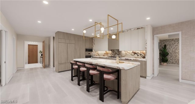 kitchen featuring wallpapered walls, an island with sink, a sink, a kitchen bar, and modern cabinets