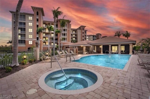 pool at dusk with a community hot tub and a patio area