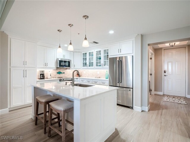 kitchen with a center island with sink, pendant lighting, appliances with stainless steel finishes, light hardwood / wood-style floors, and white cabinets