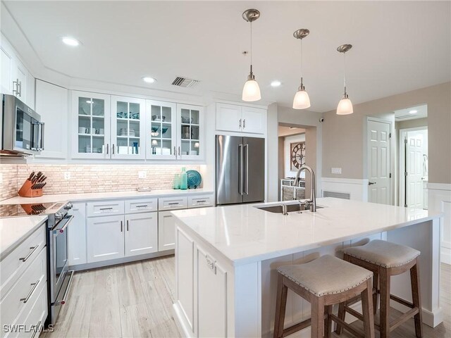 kitchen with stainless steel appliances, a center island with sink, white cabinetry, and sink