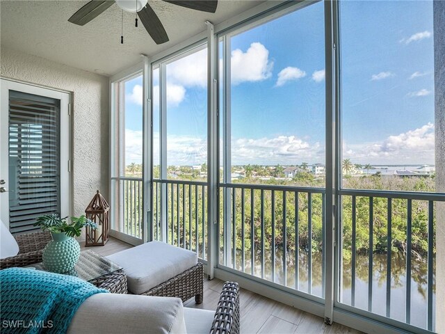 sunroom / solarium with a healthy amount of sunlight, ceiling fan, and a water view