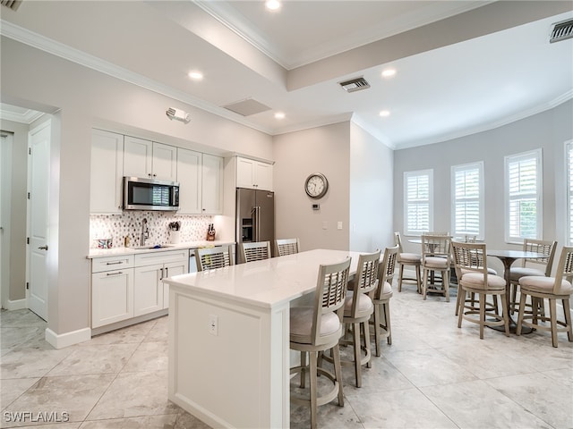 kitchen with a center island, stainless steel appliances, ornamental molding, and white cabinetry