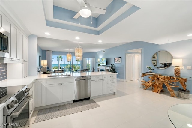 kitchen with a sink, a raised ceiling, appliances with stainless steel finishes, a peninsula, and ceiling fan