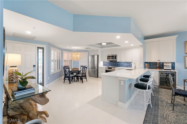 kitchen with white cabinets, wine cooler, sink, stainless steel appliances, and a kitchen bar