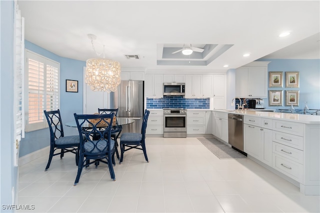 kitchen featuring hanging light fixtures, tasteful backsplash, white cabinetry, stainless steel appliances, and ceiling fan with notable chandelier