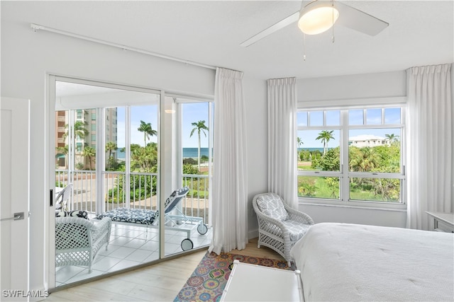 bedroom featuring ceiling fan, light hardwood / wood-style floors, access to exterior, and a water view