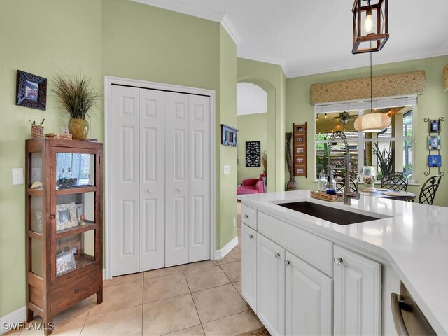 kitchen with sink, white cabinetry, crown molding, light tile patterned floors, and decorative light fixtures