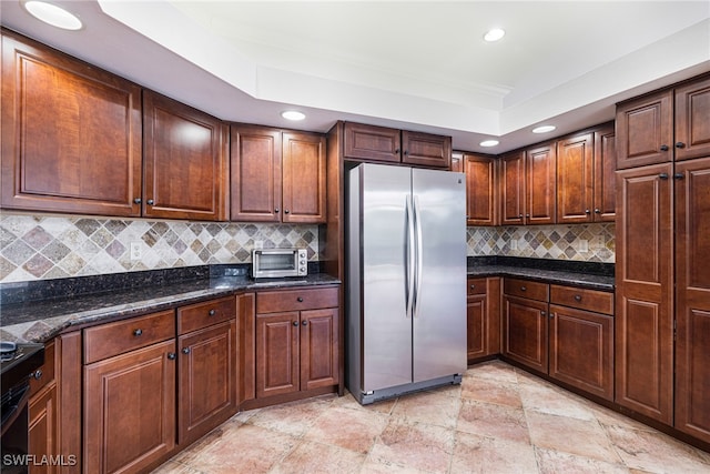 kitchen with a raised ceiling, stainless steel fridge, decorative backsplash, and dark stone counters