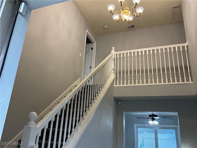 stairs featuring ceiling fan with notable chandelier