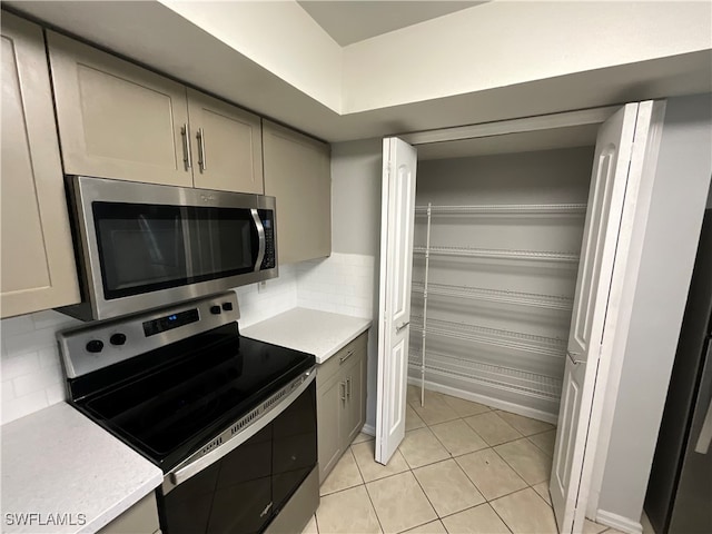 kitchen with gray cabinetry, light tile patterned floors, stainless steel appliances, and decorative backsplash