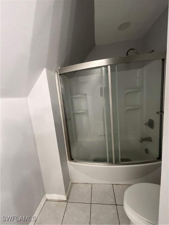 bathroom featuring toilet, bath / shower combo with glass door, and tile patterned flooring