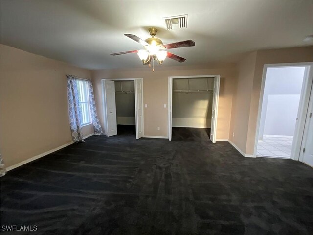 unfurnished bedroom with dark carpet, ceiling fan, and two closets