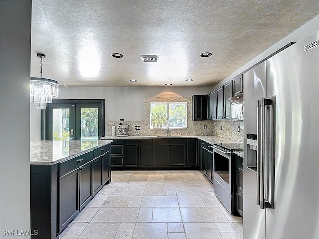 kitchen featuring appliances with stainless steel finishes, pendant lighting, light stone counters, and plenty of natural light