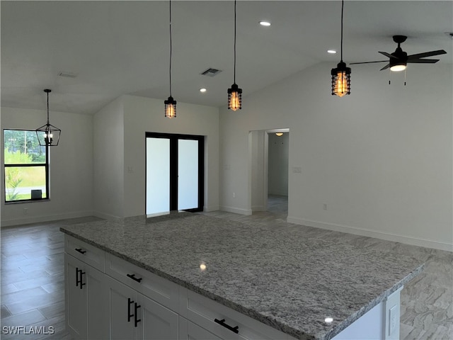 kitchen with lofted ceiling, light stone counters, white cabinets, and hanging light fixtures