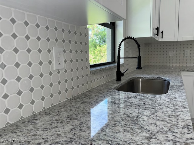 kitchen with light stone countertops, sink, white cabinets, and decorative backsplash