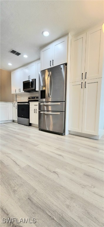 kitchen featuring appliances with stainless steel finishes, a textured ceiling, light hardwood / wood-style floors, and white cabinets