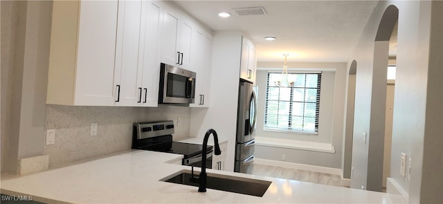 kitchen with appliances with stainless steel finishes, light hardwood / wood-style floors, white cabinetry, and decorative light fixtures