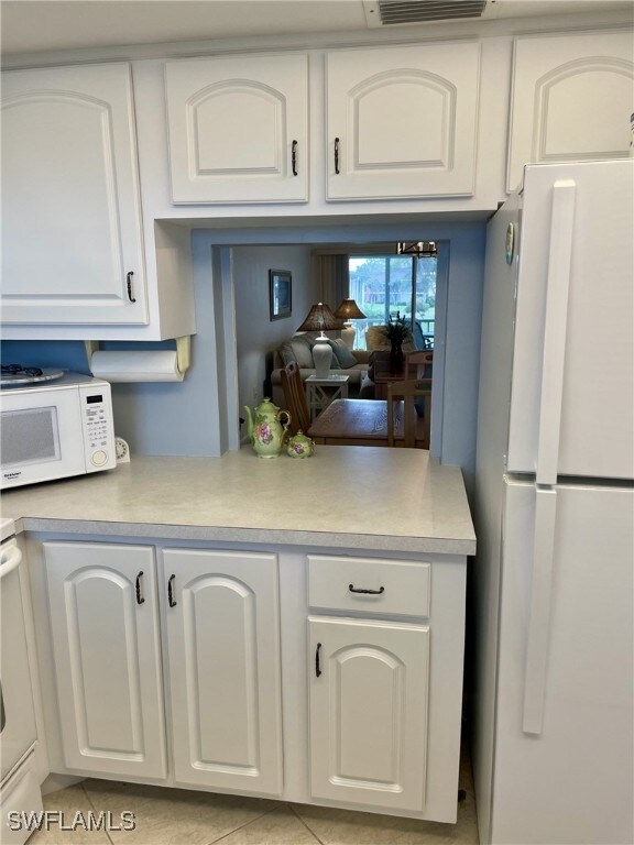 kitchen featuring white cabinets, light tile patterned flooring, and white appliances