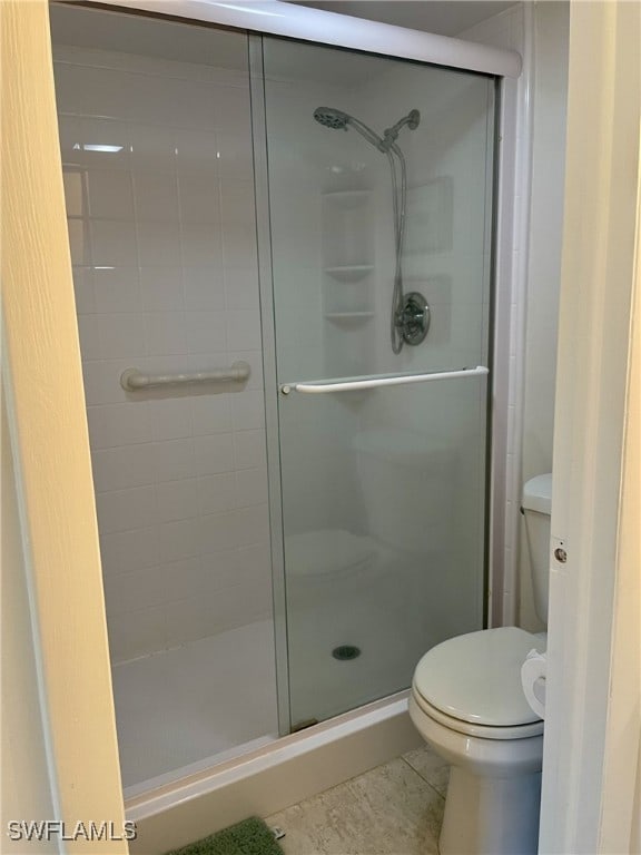 bathroom featuring toilet, a shower with shower door, and tile patterned flooring