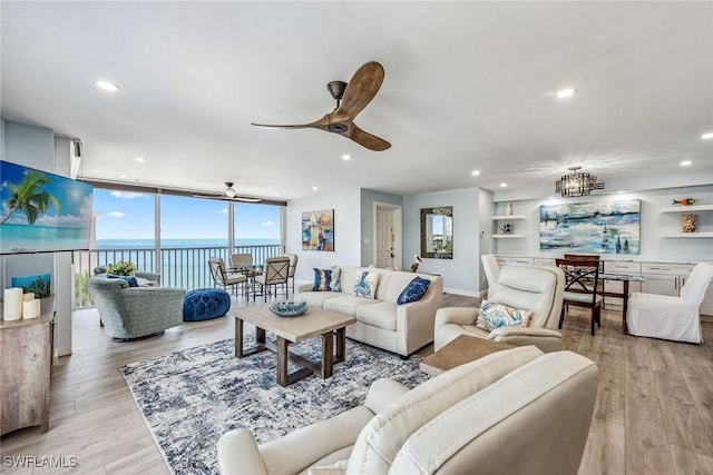 living room featuring expansive windows, ceiling fan, a water view, and light wood-type flooring