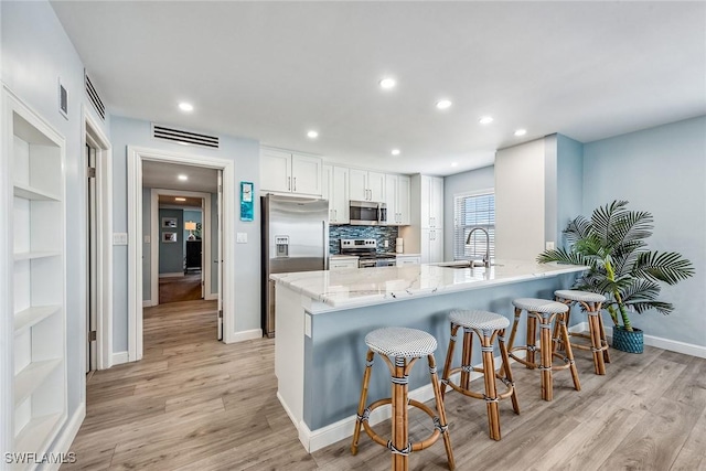 kitchen featuring white cabinets, a kitchen bar, kitchen peninsula, stainless steel appliances, and light hardwood / wood-style flooring