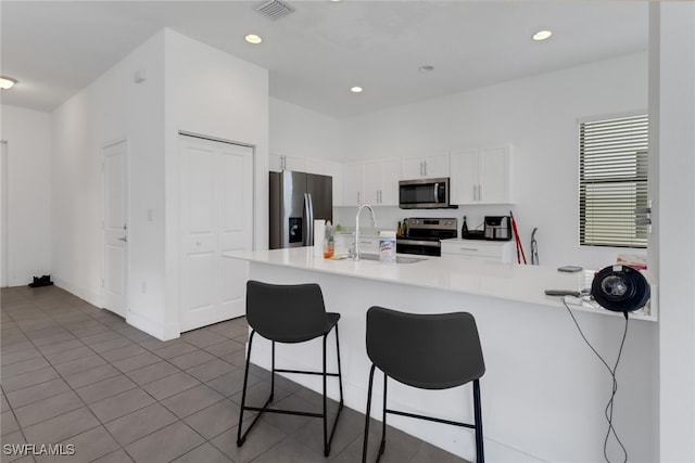 kitchen with appliances with stainless steel finishes, white cabinetry, sink, kitchen peninsula, and a kitchen bar