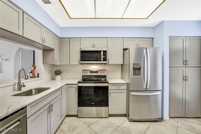 kitchen featuring gray cabinets, tasteful backsplash, sink, appliances with stainless steel finishes, and light stone countertops