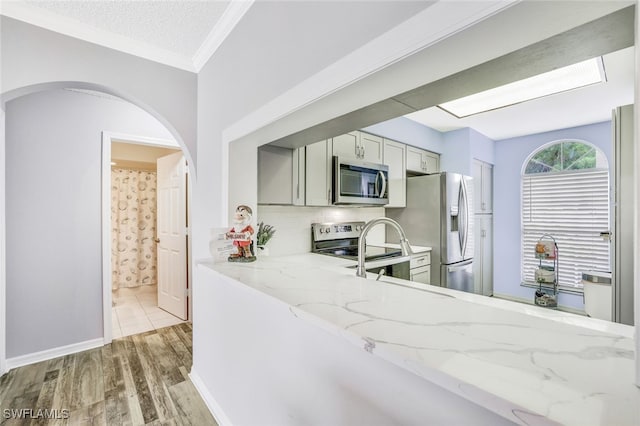 kitchen with gray cabinets, light hardwood / wood-style floors, appliances with stainless steel finishes, crown molding, and light stone countertops