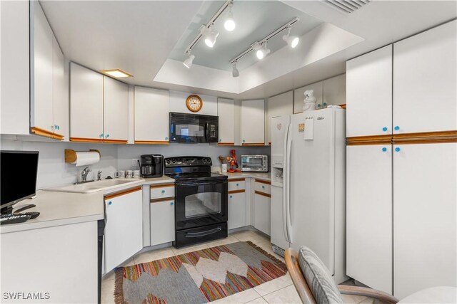 kitchen with white cabinets, light tile patterned flooring, a tray ceiling, and black appliances