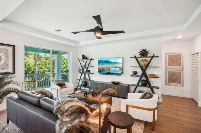 living room featuring ceiling fan, a tray ceiling, and wood-type flooring