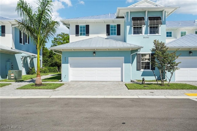 view of front of property featuring decorative driveway, central air condition unit, stucco siding, metal roof, and a garage